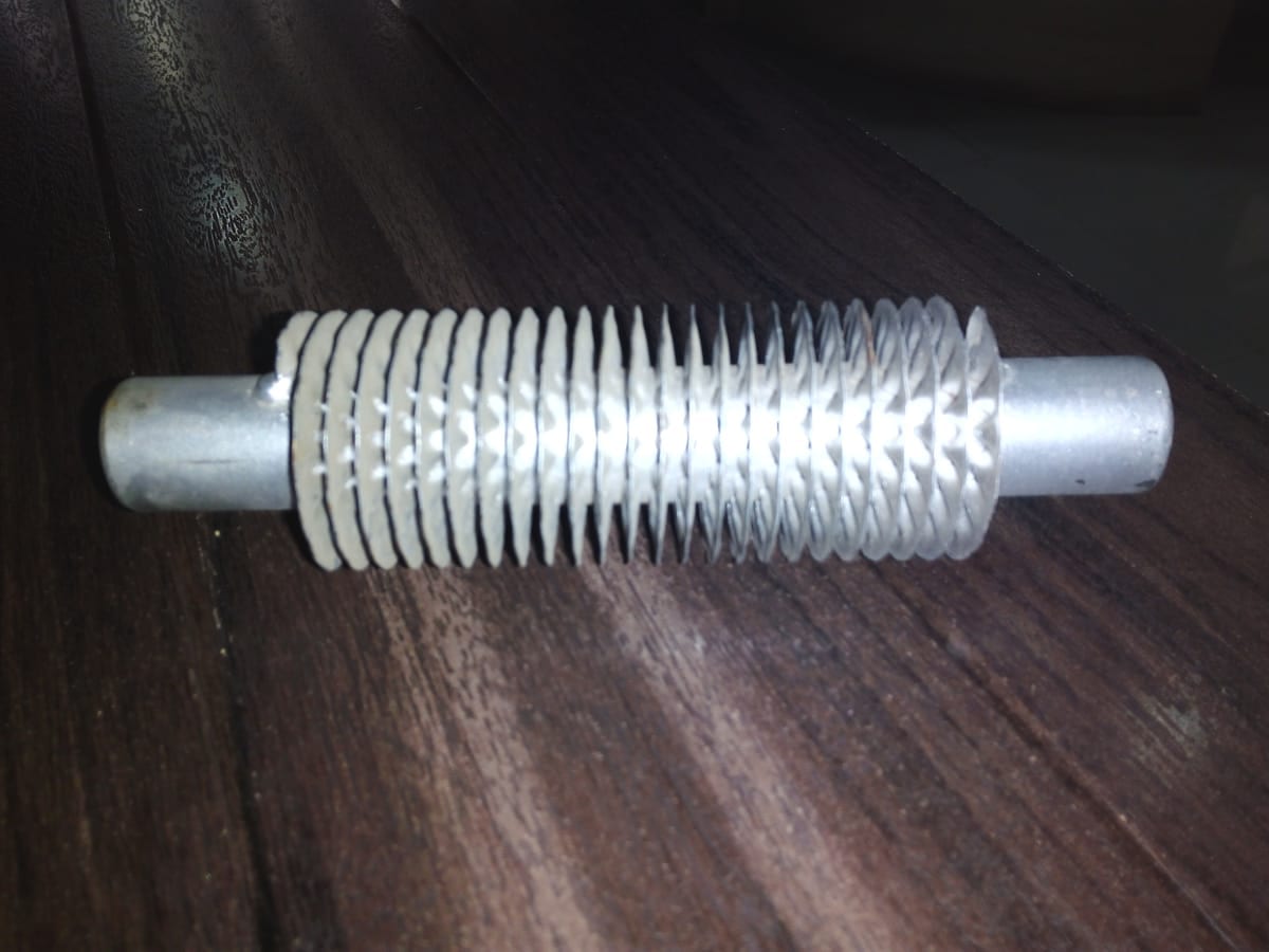 A finished fin tube, helical fin wound along its centre with plain bore left at each end, lying on a dark bench